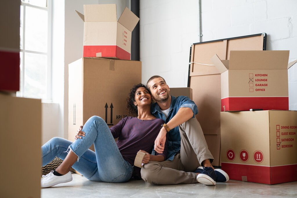 a happy first-time home buyer couple sits among moving boxes in their new home