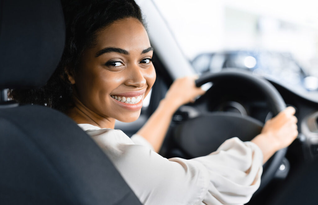 Woman driving car, smiling at camera.